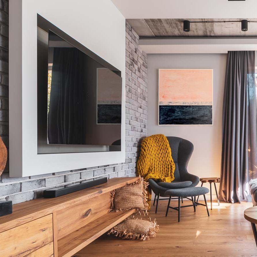 Elegant living room with light wooden floor, grey couch and wing back chair and big tv on the wall